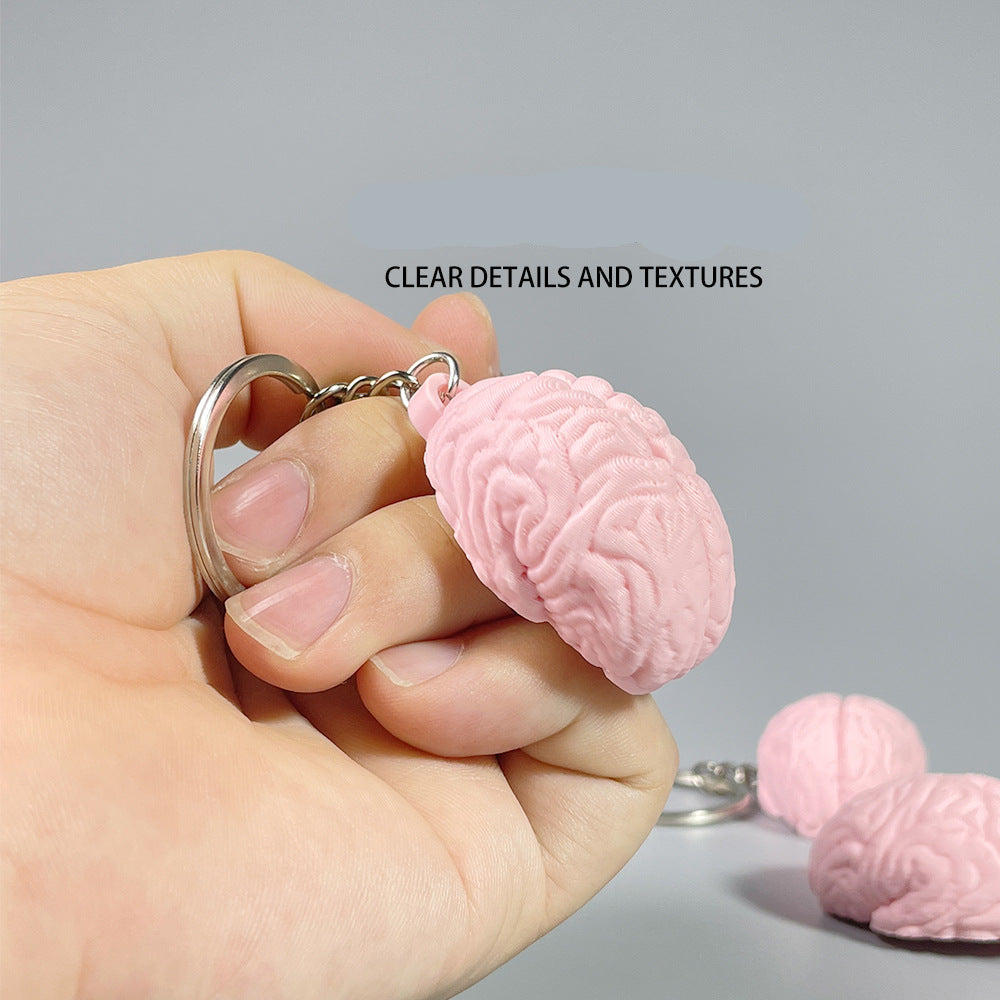 Pink brain-shaped keychain held in a hand with a gray background
