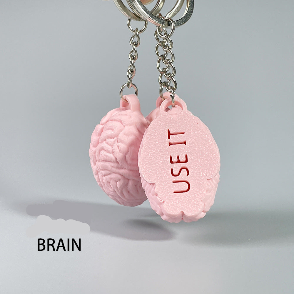 Pink brain-shaped keychain with 'USE IT' text on a gray background