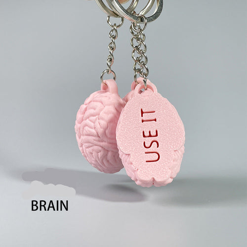 Pink brain-shaped keychain with 'USE IT' text on a gray background